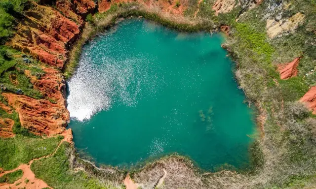 Lago turchese circondato da rocce rosse e vegetazione rigogliosa, un paesaggio suggestivo che ricorda le cave di bauxite.