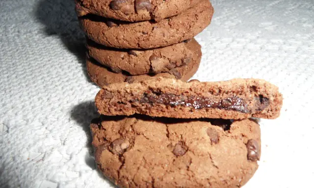 Gros plan sur une pile de biscuits au chocolat, dont un est coupé en deux révélant un cœur coulant de Nutella. Une recette de biscuit Nutella parfaite pour les gourmands.