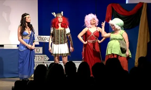 Attrici in costume su un palco, forse per la lisistrata trama. Una in blu, una guerriera, una con capelli rosa e una in verde.