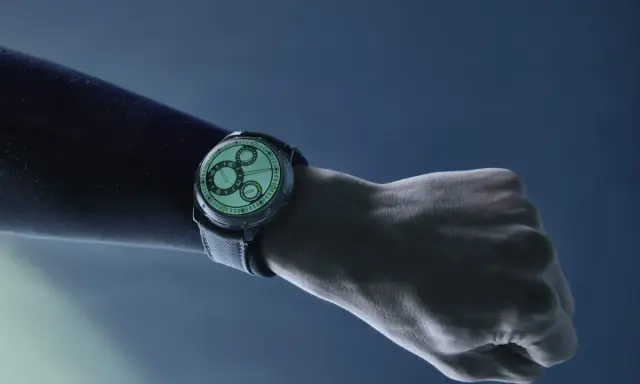 Un polso con un orologio dal quadrante luminoso, con indici e lancette che brillano grazie al super luminova, su sfondo blu scuro.