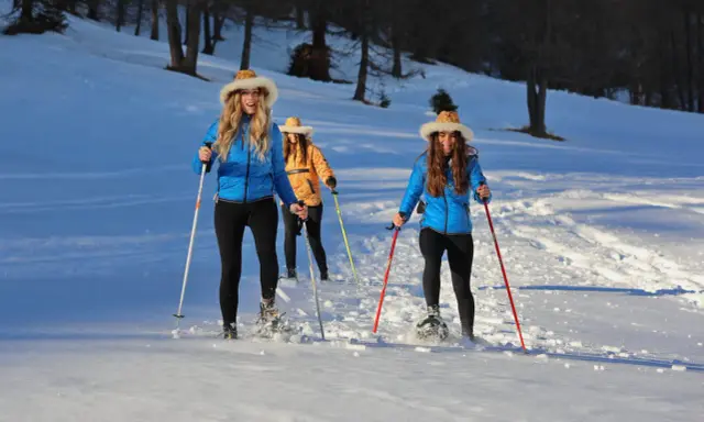 Tre amiche si godono escursioni invernali nelle Dolomiti Bellunesi, camminando sulla neve con le ciaspole e bastoncini.