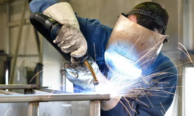 Soldador con máscara y guantes, demostrando cómo soldar con electrodo, creando chispas brillantes.