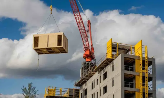 Une grue rouge soulève un module en bois pour la construction hors site d'un bâtiment en béton.