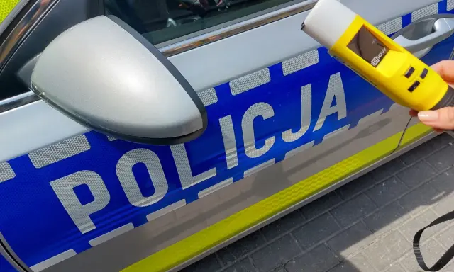 Policjantka trzyma alkomat przy radiowozie. Wynik 13.7 promila to nierealny, ale symboliczny wynik dla kierowcy pod wpływem alkoholu.