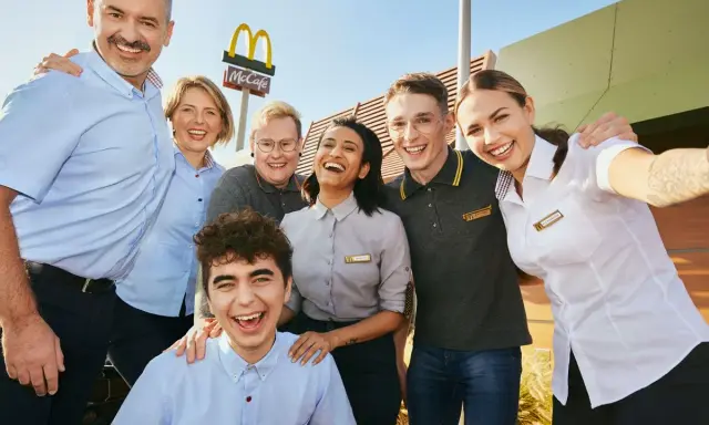 Uśmiechnięty zespół McDonald's, gotowy do pracy. W tle logo McCafe.