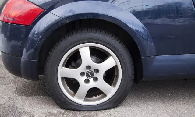 Ruota posteriore di un'auto blu con evidente perdita pressione pneumatici. Il pneumatico è sgonfio e appoggiato a terra.