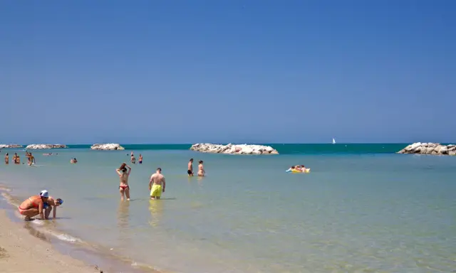 Persone si godono una giornata di sole sulla spiaggia libera di Torre Pedrera, tra bagni e relax in mare.