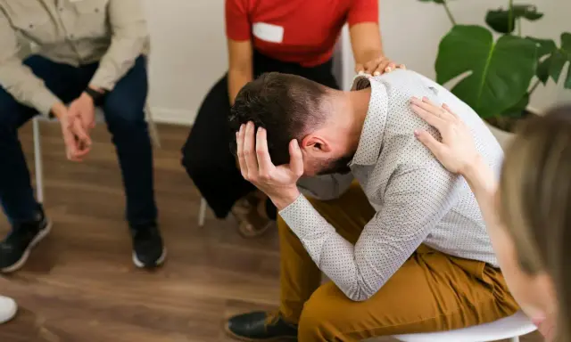 Grupa wsparcia dla osób walczących z nałogiem. Mężczyzna w centrum trzyma się za głowę, czując się przytłoczony.