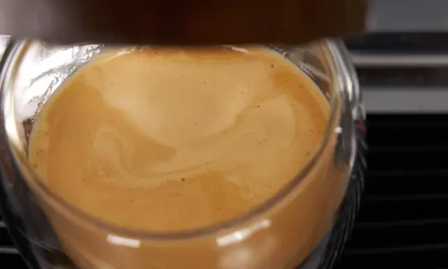 Ein Glas mit cremigem Kaffee, das ist cafe crema mit milch. Die goldbraune Crema wirbelt sanft.