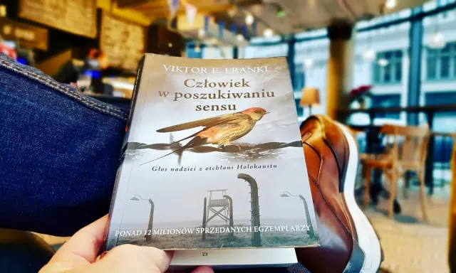 Osoba czyta "Człowiek w poszukiwaniu sensu" Viktora Frankla, szukając nadziei i znaczenia w trudnych czasach.