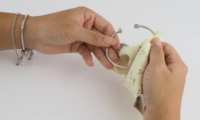 Manos puliendo un brazalete de plata con un paño. Aprende como limpiar cadena de plata y mantener tus joyas brillantes.