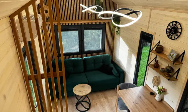 Przytulne wnętrze tiny house Polska: zielona kanapa, drewniane meble i nowoczesne oświetlenie. Idealne miejsce na relaks.
