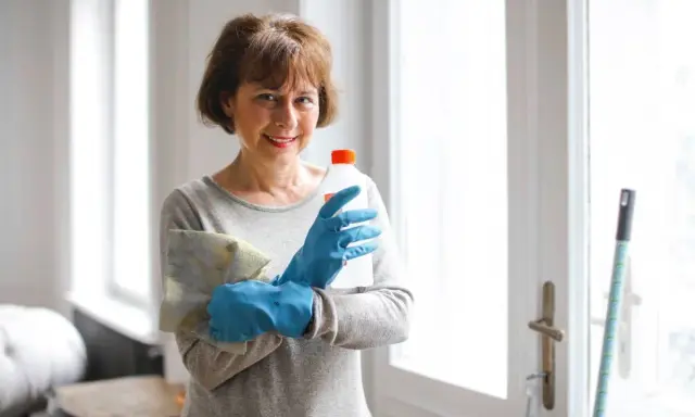 Mujer con guantes azules, paño y botella de limpiador, lista para saber como limpiar un colchon de viscoelastica.