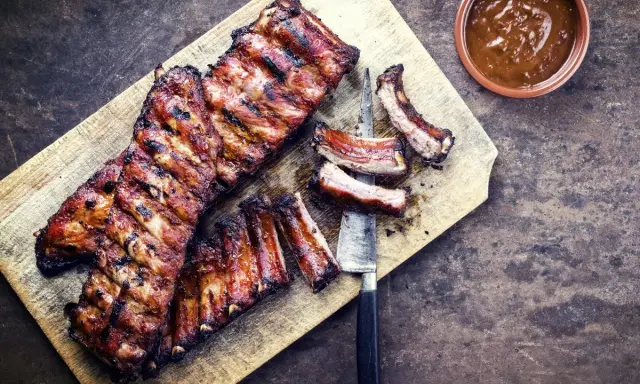 Soczyste żeberka w miodzie, grillowane do perfekcji, leżą na desce obok sosu.