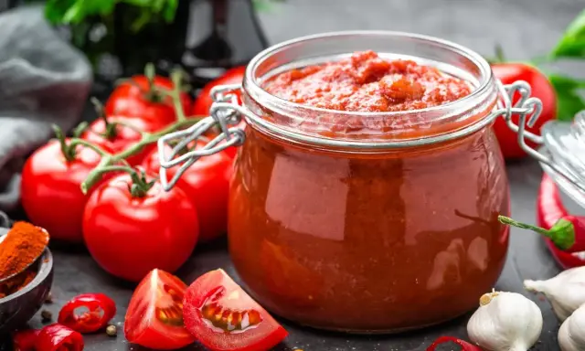 Słoik przecieru pomidorowego, świeże pomidory, czosnek i papryczki chili. Pasteryzacja przecieru pomidorowego w piekarniku to świetny sposób na jego przechowywanie.