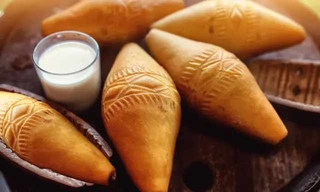 Kilka oscypków z ozdobnymi wzorami i szklanka mleka na drewnianym tle.