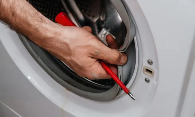 Mano con destornillador limpiando la goma de la lavadora. Aprende como quitar el moho de la goma de la lavadora para un mejor lavado.