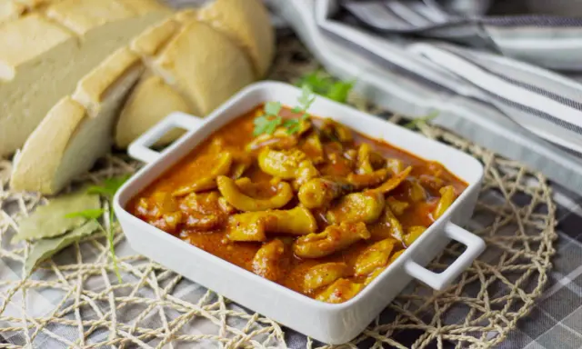 Deliciosa jibia en salsa, servida en un cuenco blanco, acompañada de pan rústico y decorada con perejil.