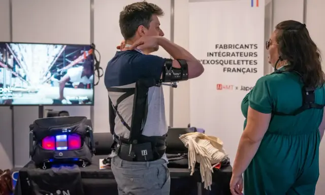 Un homme teste un exosquelette pour le bras, une technologie d'assistance pour le handicap. Une femme observe.