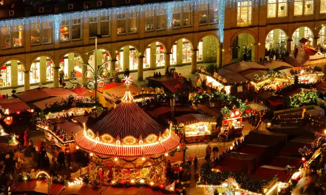 Vista aérea de mercadillos navideños iluminados, con un carrusel festivo y puestos de comida.