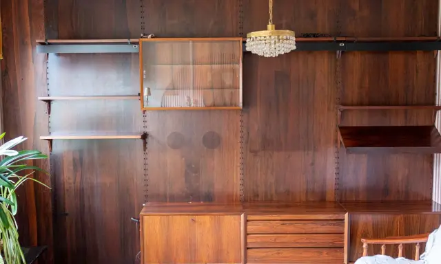 En väggmonterad hylla i teak, troligen designad av Poul Cadovius, med glasmonter, lådor och hyllplan.