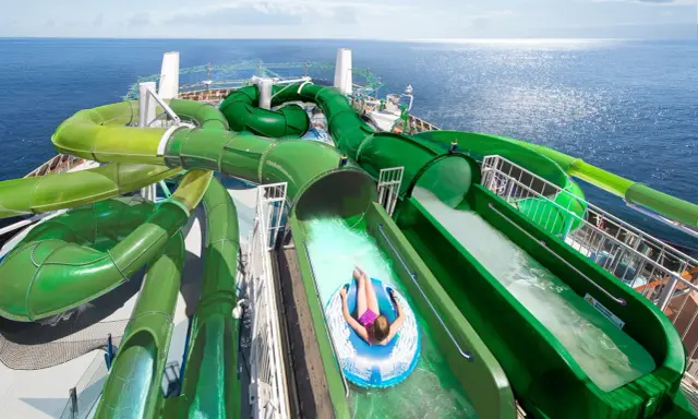Divertente crociera per bambini con scivoli acquatici verdi che si snodano sul ponte di una nave da crociera, con il mare blu sullo sfondo.