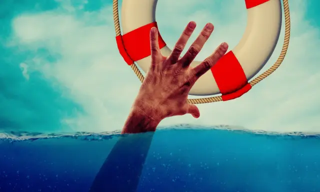 Dłoń wyciągnięta z wody chwyta koło ratunkowe. To symbol nadziei i szansy na nowe życie, jak w przypadku wczasów odwykowych dla alkoholików.