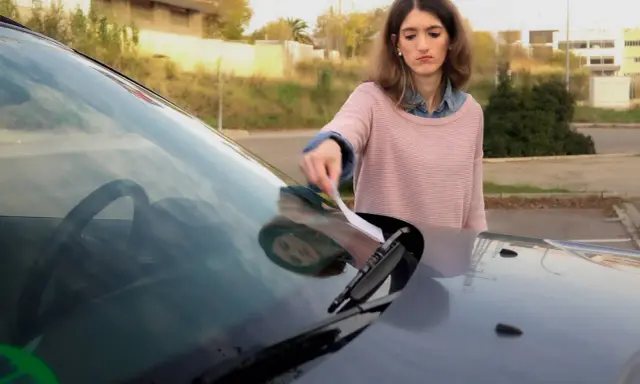 Mujer saca papel del parabrisas, preocupada por como saber si me han multado.
