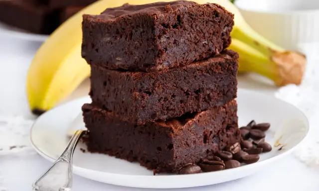Stos puszystych brownie z bananami, ozdobiony ziarnami kawy, na talerzu z bananem w tle.