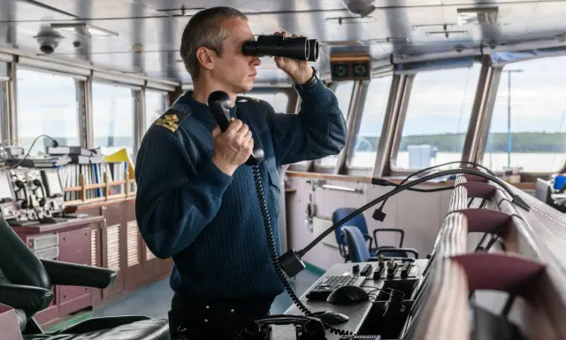 Un officier de marine, comment s'appelle la personne qui conduit un bateau, utilise des jumelles et un téléphone dans la passerelle.