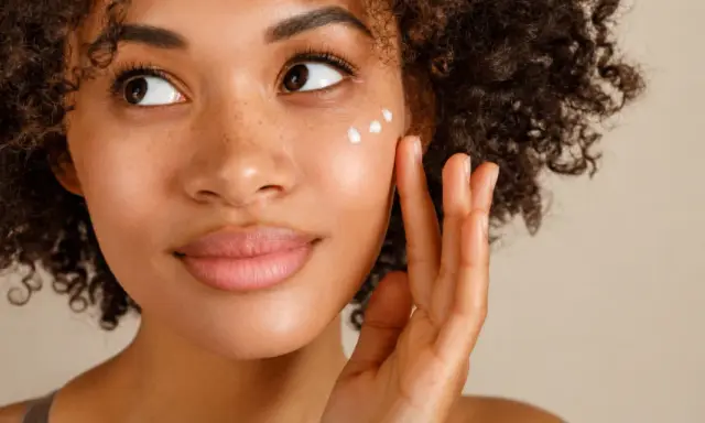 Donna con capelli ricci applica crema sul viso per una pelle bella e luminosa.