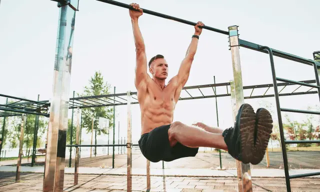 Uomo muscoloso esegue un esercizio di calisthenics per principianti alla sbarra, sollevando le gambe.