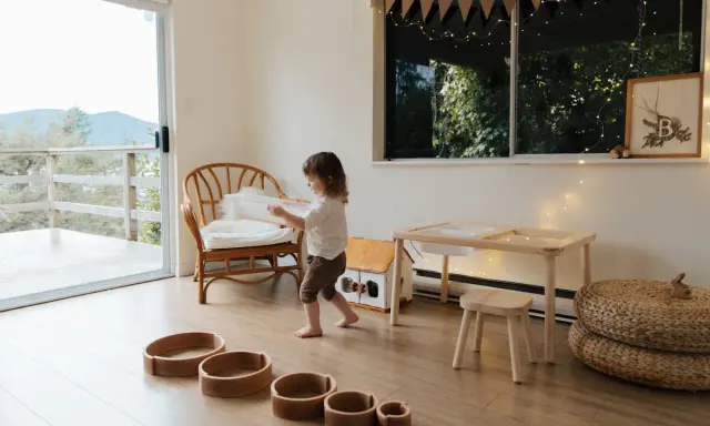 Bambina gioca in una stanza giochi in casa, tra sedie di vimini, tavolino e cesti.