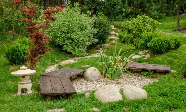 Un paisible petit jardin japonais avec des lanternes, des bancs en bois, des rochers et une végétation luxuriante.