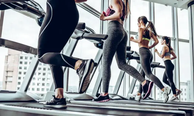 Kobiety ćwiczą cardio na bieżni, biegnąc w siłowni z widokiem na miasto.