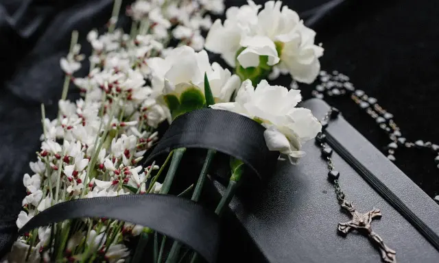 Białe kwiaty na pogrzeb, czarna wstęga i różaniec na czarnej tkaninie. Symbol żałoby i pamięci.