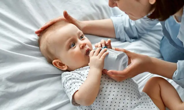 Maluch szarpie się przy karmieniu butelką, ale mama cierpliwie go uspokaja.