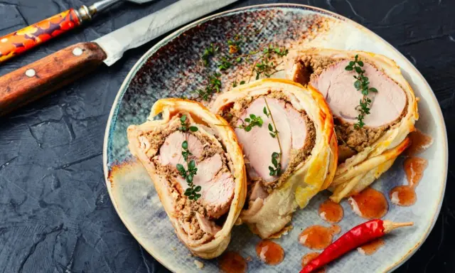 Pyszne danie z ciasta francuskiego z soczystym mięsem i farszem grzybowym, udekorowane gałązkami tymianku i papryczką chili.