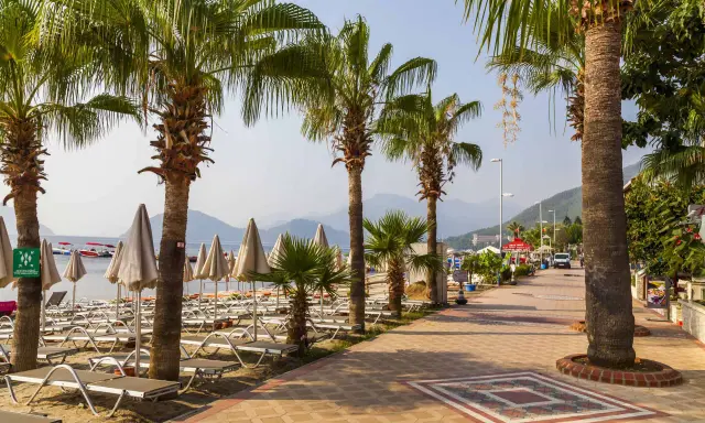 Alejka z palmami prowadzi do plaży w Marmaris, Turcja. Leżaki i parasole czekają na turystów.