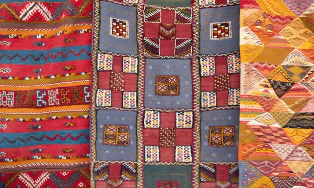 Bunte Teppiche mit geometrischen Mustern, die das orientalische Flair widerspiegeln. Ein Teppich zeigt Streifen, ein anderer Quadrate und das dritte Rauten.