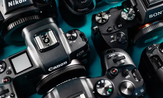 Zbliżenie na kilka nowoczesnych bezlusterkowców marek Nikon, Canon i Sony, ułożonych na turkusowym tle.