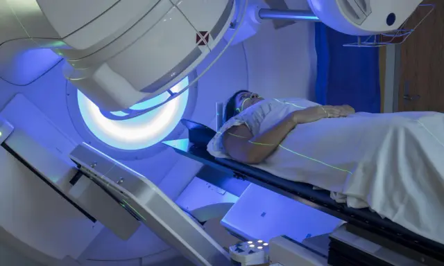 Pacjentka leży na stole terapeutycznym pod aparatem do radioterapii. Zielone linie laserowe wyznaczają pole napromieniania. To właśnie radioterapia co to jest – nowoczesna metoda leczenia.
