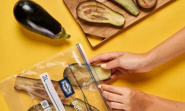 Hände legen Auberginenscheiben in einen Gefrierbeutel. So einfach ist das Aubergine einfrieren für später.