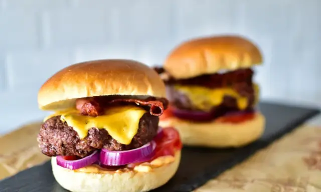 Zwei saftige Burger im Airfryer zubereitet, mit geschmolzenem Käse, knusprigem Speck und roten Zwiebeln.