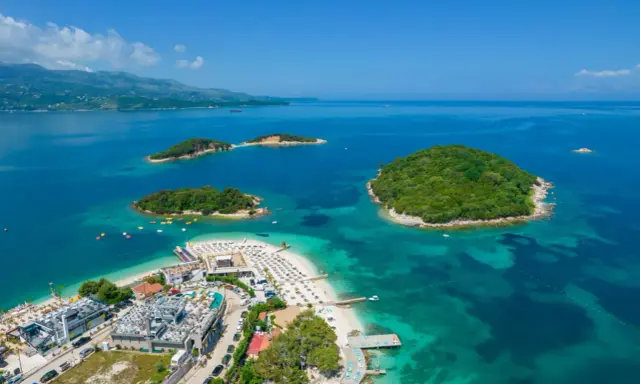Malownicze wyspy otoczone turkusowym morzem, z piaszczystą plażą i nowoczesnymi budynkami. To raj na ziemi: Albania, plaża Ksamil.