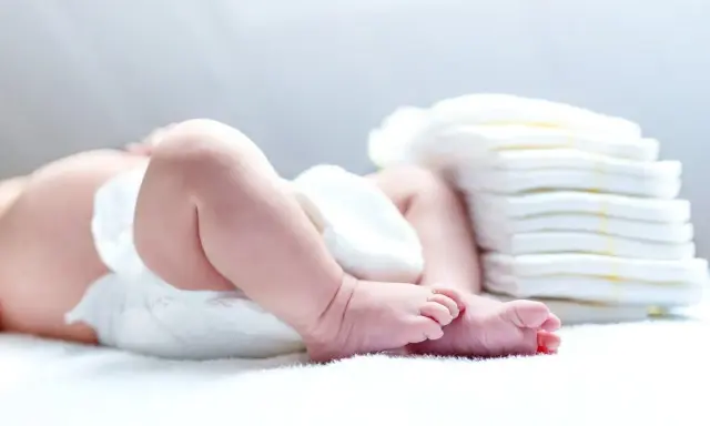 Nietolerancja laktozy u niemowlaka? Śluz w kupie może być sygnałem. Na zdjęciu nóżki dziecka i stos pieluch.