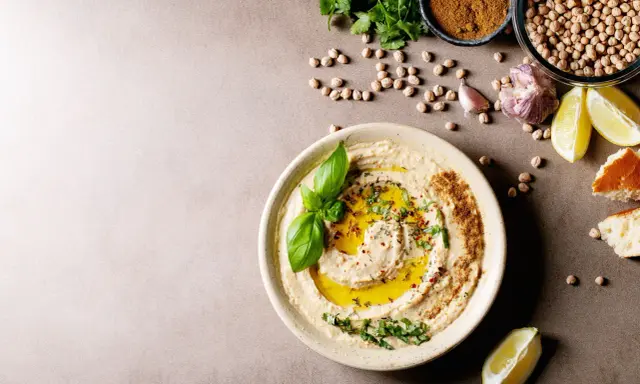 Pyszny hummus z oliwą, ziołami i bazylią. Obok ciecierzyca, czosnek, cytryna i chleb. Czy można mrozić hummus? Tak, można go mrozić.