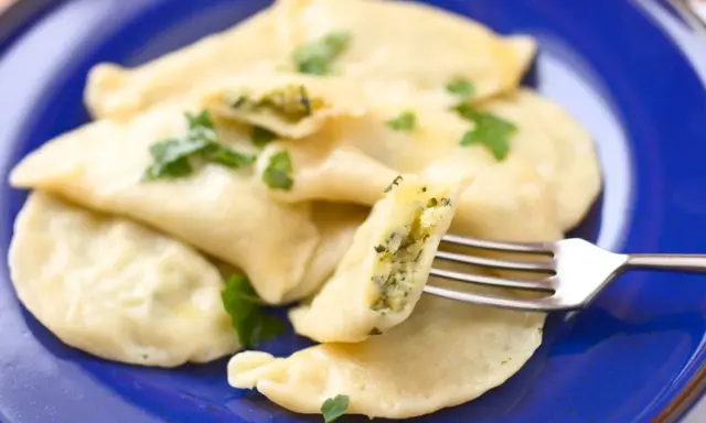 Pyszne pierogi ze szpinakiem, polane masłem i posypane natką pietruszki, czekają na widelcu.