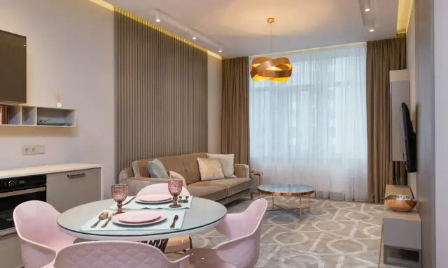 Nowoczesny salon z aneksem kuchennym po generalnym remoncie mieszkania 50m2. Jasne kolory, welurowa sofa i różowe krzesła tworzą przytulną atmosferę.