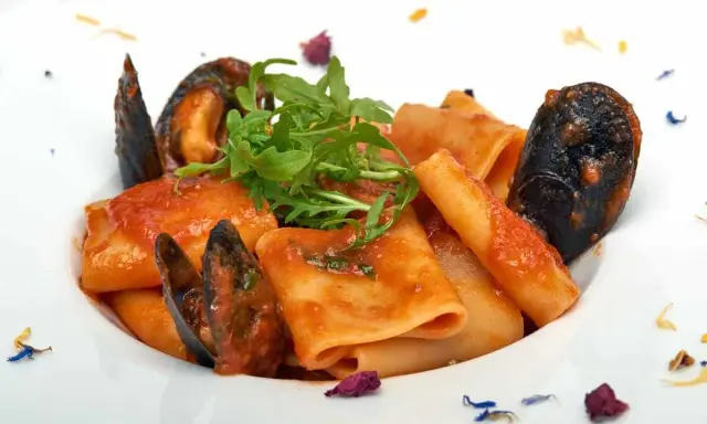 Paccheri allo scoglio con cozze e pomodoro, guarniti con rucola fresca e petali di fiori.
